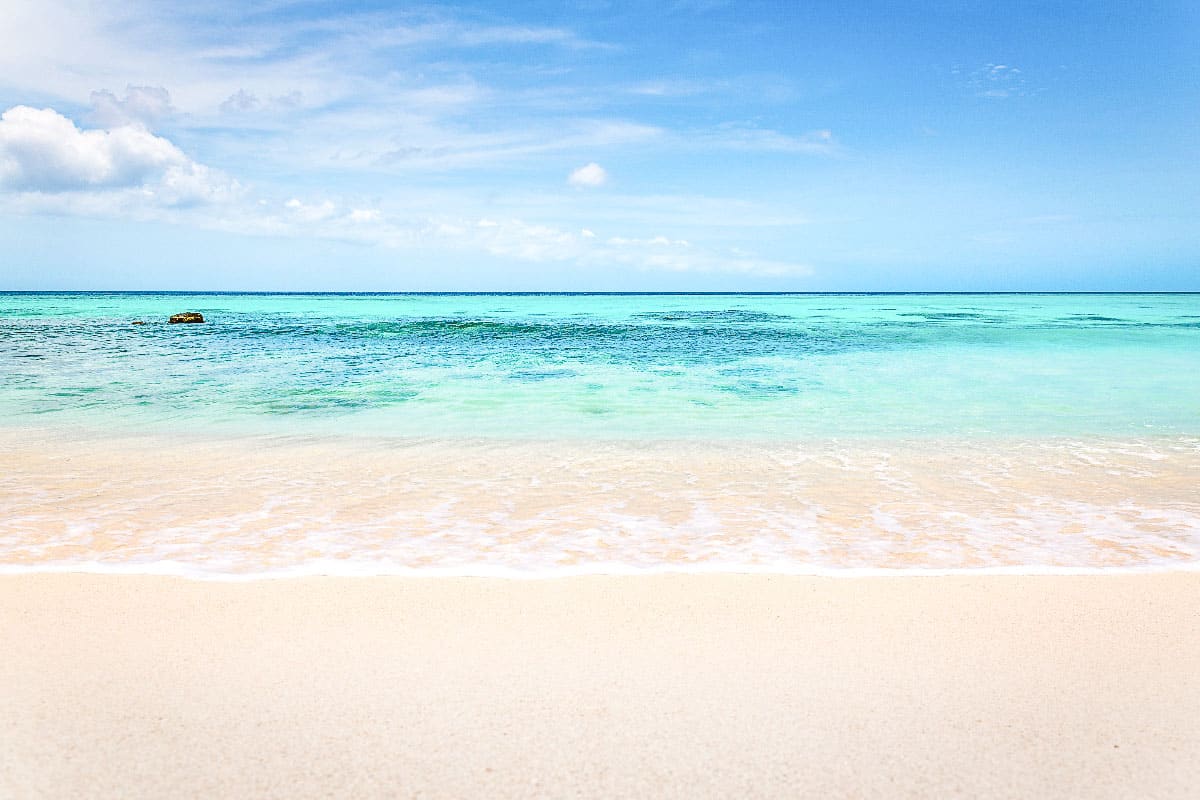 Pristine sandy beach meeting the crystal-clear turquoise waters of a calm sea, under a beautiful sky with soft clouds, creating a serene tropical scene. You can find this beach on Klein Bonaire, amazing thing to do from bonaire cruise port