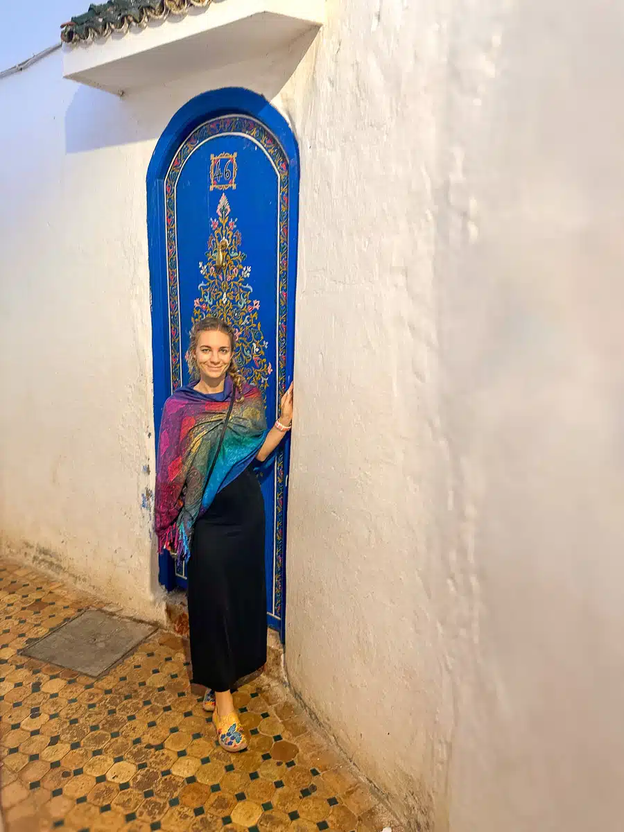 the author in a traditional scarf in front of a decorated blue door in rabat