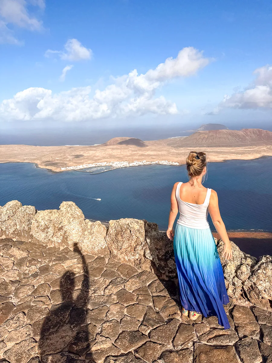 A woman looks out from Mirador del Rio in Lanzarote, her blue skirt matching the sea below, with a stunning view of La Graciosa island and the azure waters."
