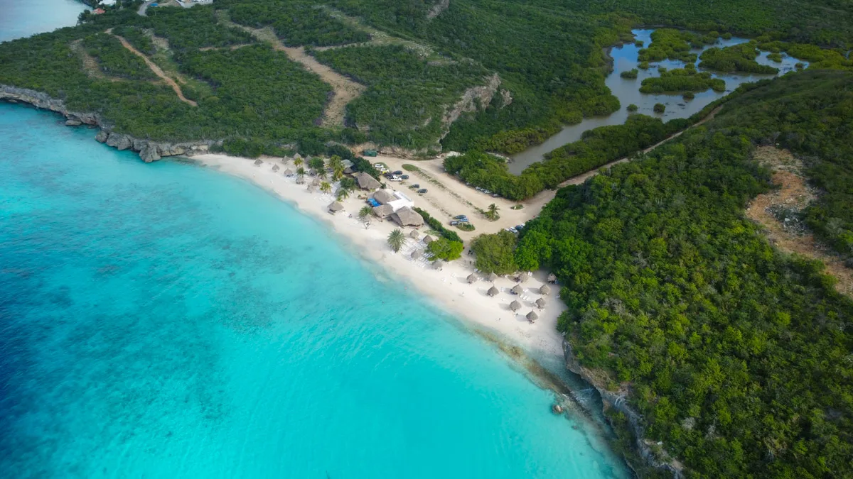 A stunning aerial shot of Cas Abao Beach in Curaçao, with its clear turquoise waters, white sandy beach, and lush greenery, inviting visitors for a swim or a snorkeling adventure.