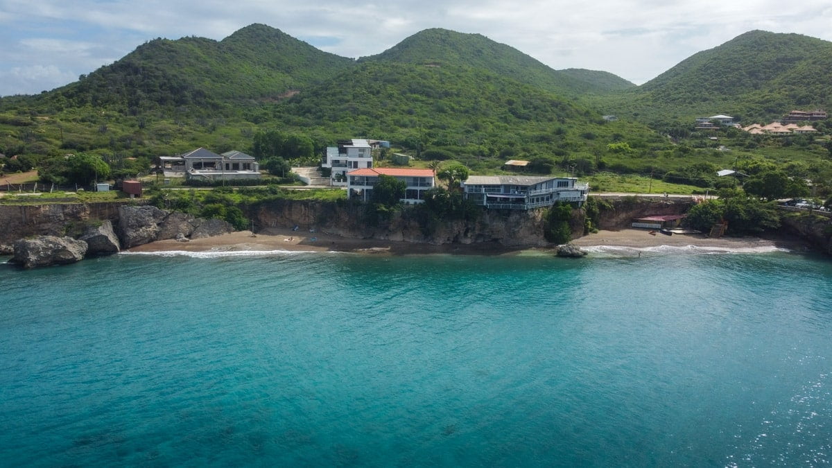 "Coastal luxury houses perched on Curaçao's cliffside offer a breathtaking view of the cove and azure sea, showcasing the island's upscale accommodation options.