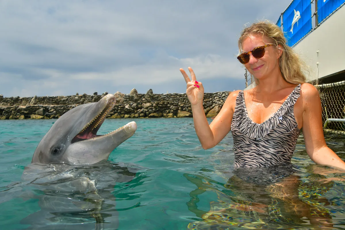 The author, sporting sunglasses, shares a joyful moment with a friendly dolphin in the clear shallow waters off Mambo Beach in Curaçao.