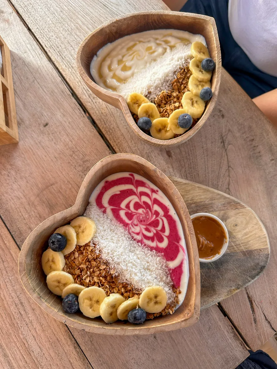 A top-down view of two delicious açaí bowls, artistically presented on a wooden table, ready to be enjoyed on a sunny day at Mambo Beach in Curaçao.