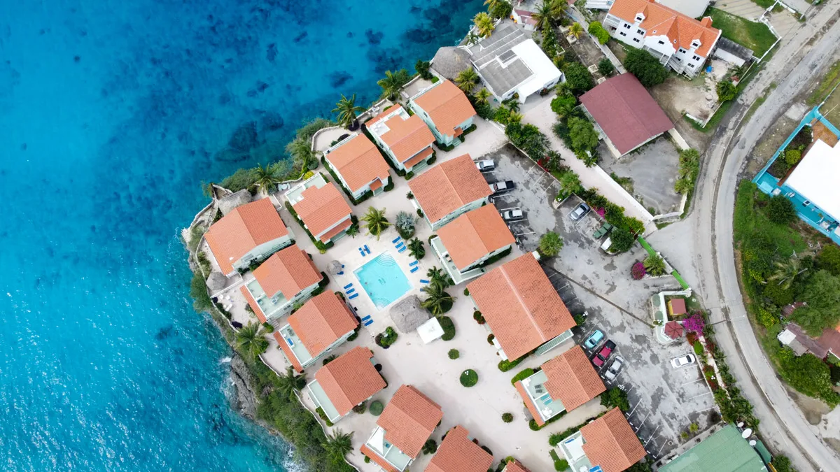The top-down view of a peaceful Curacao neighborhood, with rows of terracotta-roofed villas surrounding a communal pool, just steps away from the inviting blue sea, perfect for dive resort visitors.