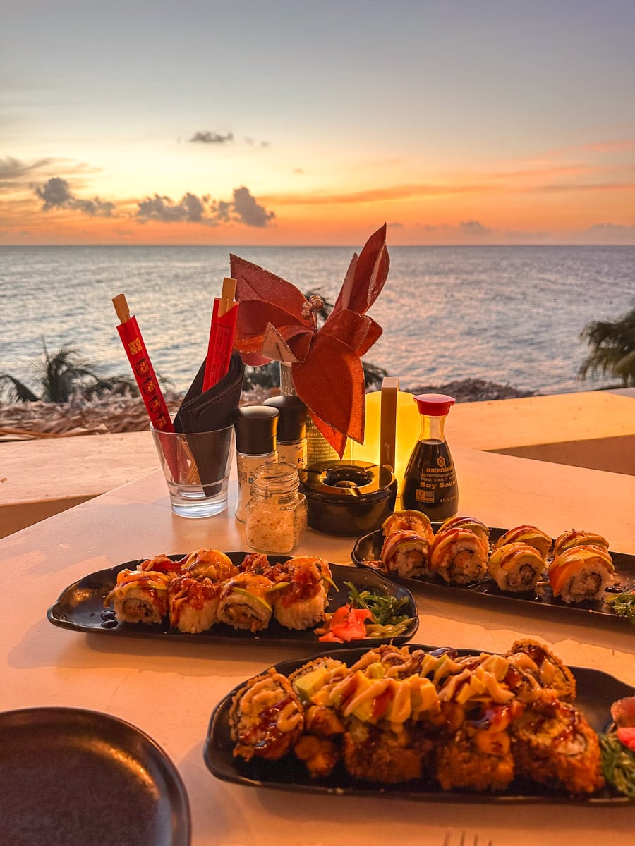A romantic dinner setting in Curaçao features an array of sushi rolls presented against the backdrop of a breathtaking sunset over the Caribbean Sea.