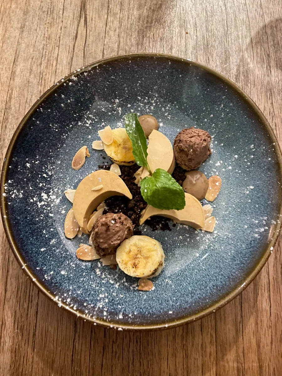 An elegantly plated dessert featuring chocolate truffles, banana slices, and almond flakes, offering a glimpse into Curaçao's culinary delights that the author might savor.