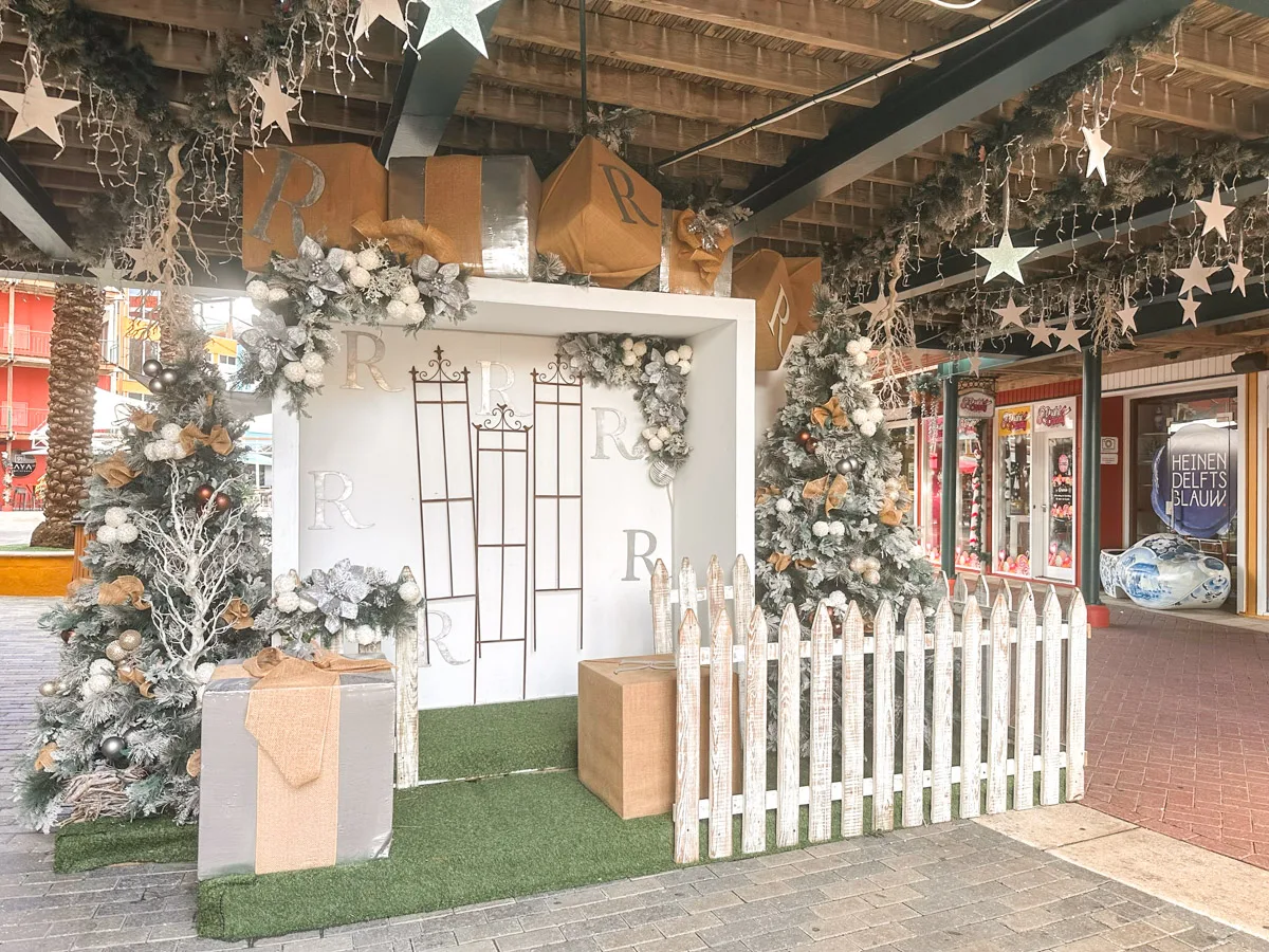 A stylish Christmas photo booth setup with silver and white decorations, stars, and wrapped gift boxes, inviting passersby to capture holiday memories.