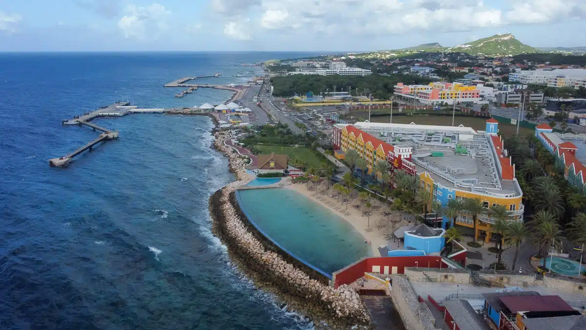 A panoramic view of a bustling Curacao cruise port with colorful buildings and a protected cove, highlighting the vibrant atmosphere of a popular dive resort destination. You can also see the artificial beach of the Renaissance Wind Creek Resort in Curacao