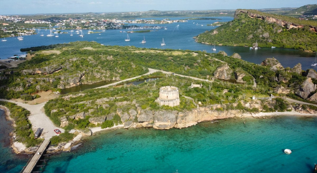 An aerial view of the historic Fort Beekenburg in Curaçao, surrounded by lush greenery and overlooking the turquoise waters of the Caribbean Sea, a testament to the island's rich history