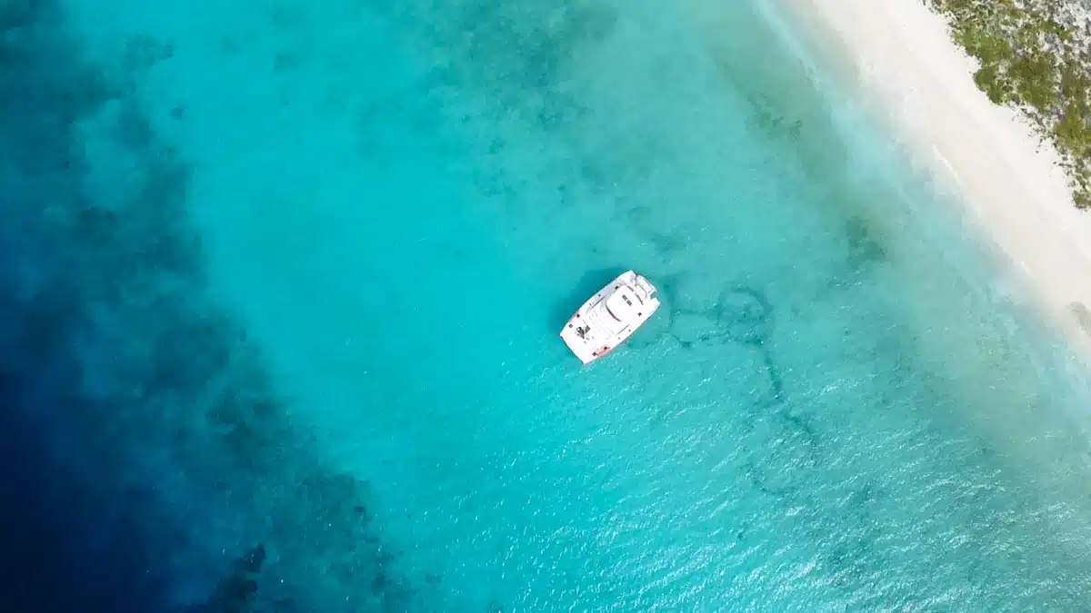 A wider aerial shot of a boat on the turquoise blue waters near a lush, deserted island, showcasing an ideal location for Klein Curacao boat trips.