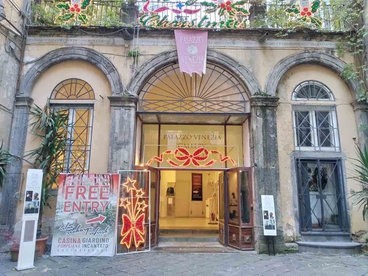 The entrance to Palazzo Venezia in Naples, adorned with Christmas decorations, inviting passersby to explore the cultural exhibitions within the historic building
