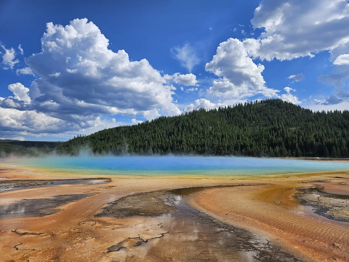 amazing spot everyone needs to visit in the us the yellowstone national park with stunning lake and orange and yellow stones in front of it