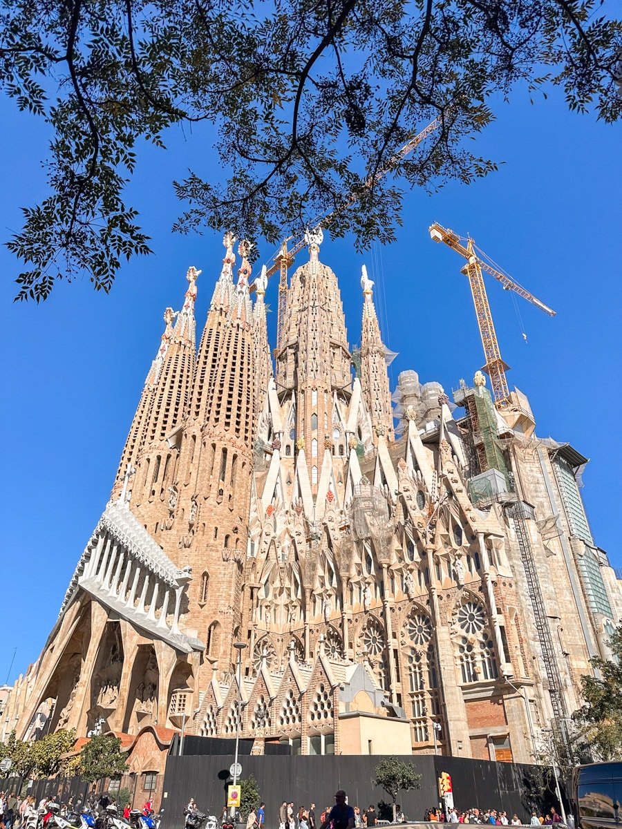 A full view of the Sagrada Familia's intricate façade, showcasing its Gothic and Art Nouveau styles, under the bright Barcelona sun