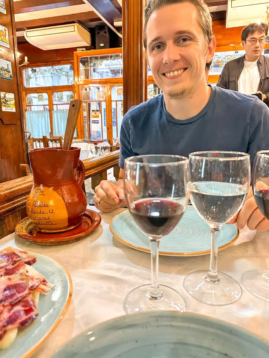 A happy traveler sampling local Spanish wine and tapas, including Iberian ham and Manchego cheese, in a cozy Barcelona restaurant