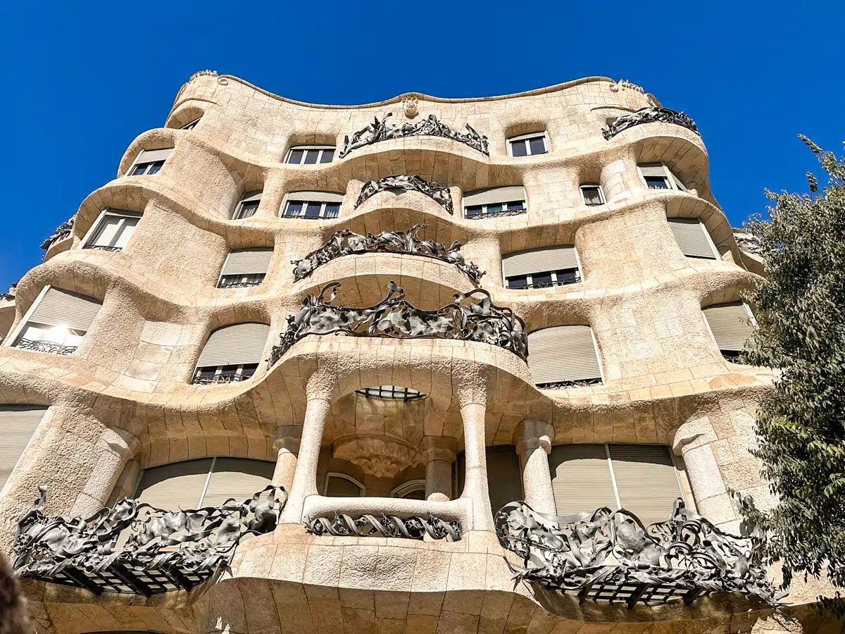 The undulating stone façade and wrought-iron balconies of Gaudí's La Pedrera, under a clear sky, reflecting Barcelona's modernist architecture.