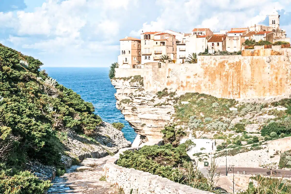 A coastal town perched atop sheer cliffs with fortified walls, overlooking a serene blue sea under a clear sky.
