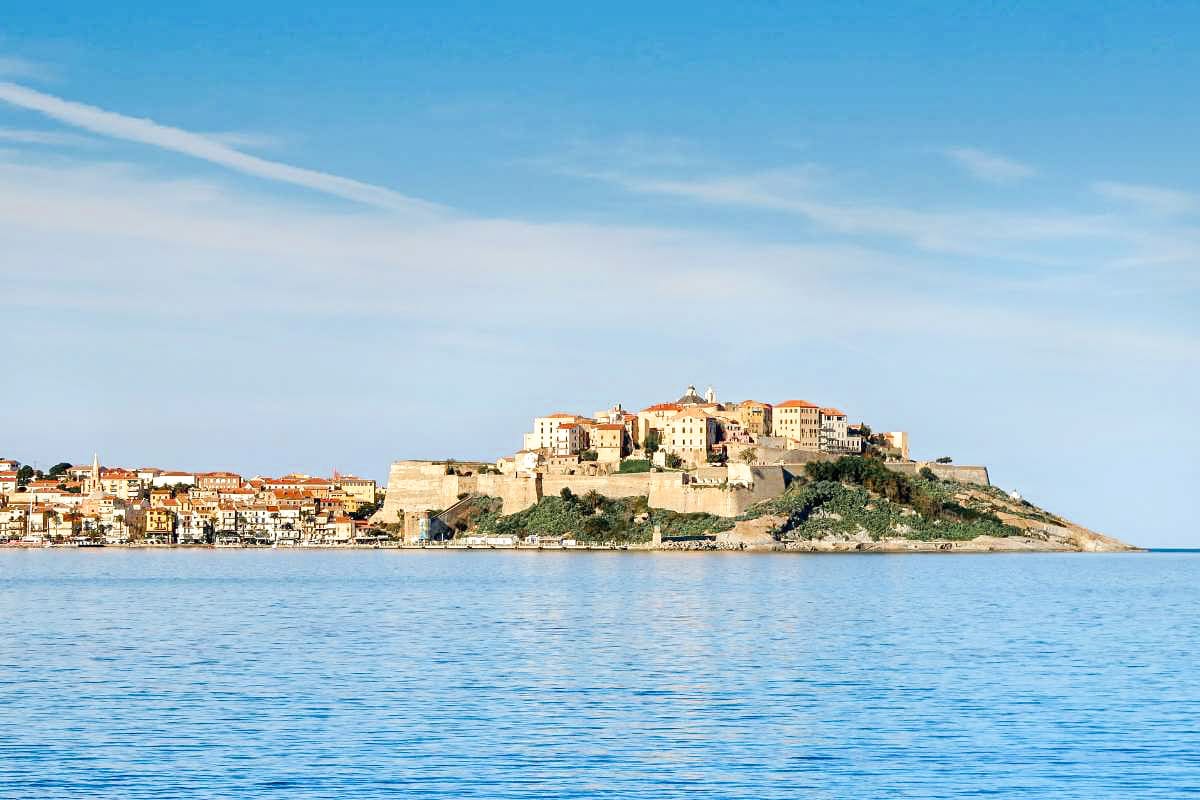 A historic clifftop town with old buildings and a church, overlooking the deep blue sea, under a partly cloudy sky.