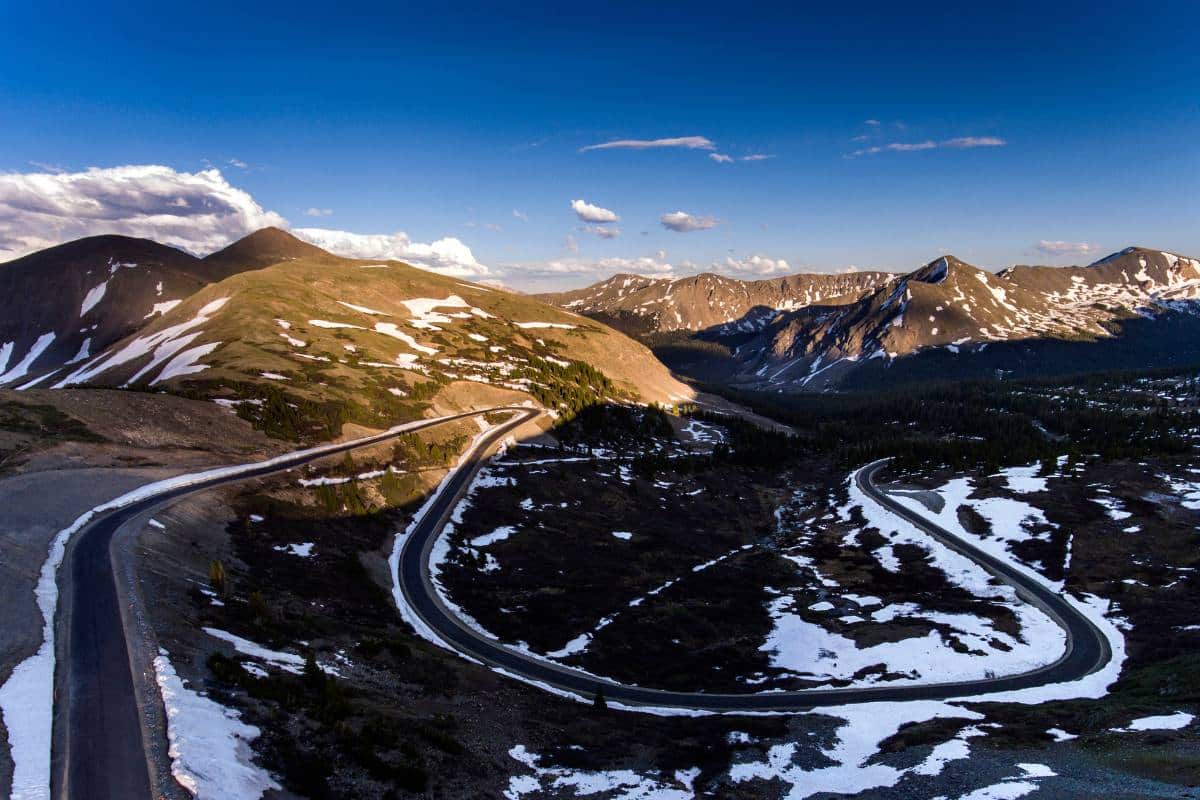 A winding road through Independence Pass near Aspen, with remaining snow patches and mountain ranges under a sunset sky.