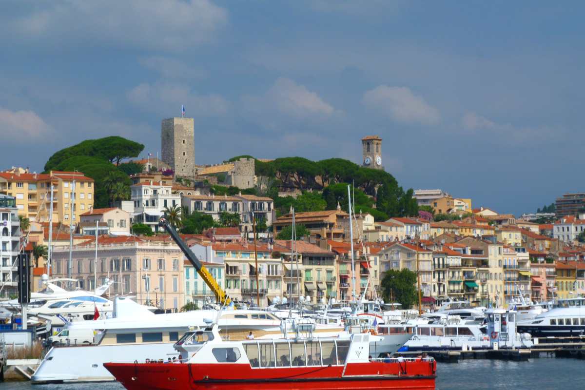 The Old Port of Cannes, with traditional and modern boats anchored in the harbor, overlooked by the historic Le Suquet area with its old castle and the clock tower.