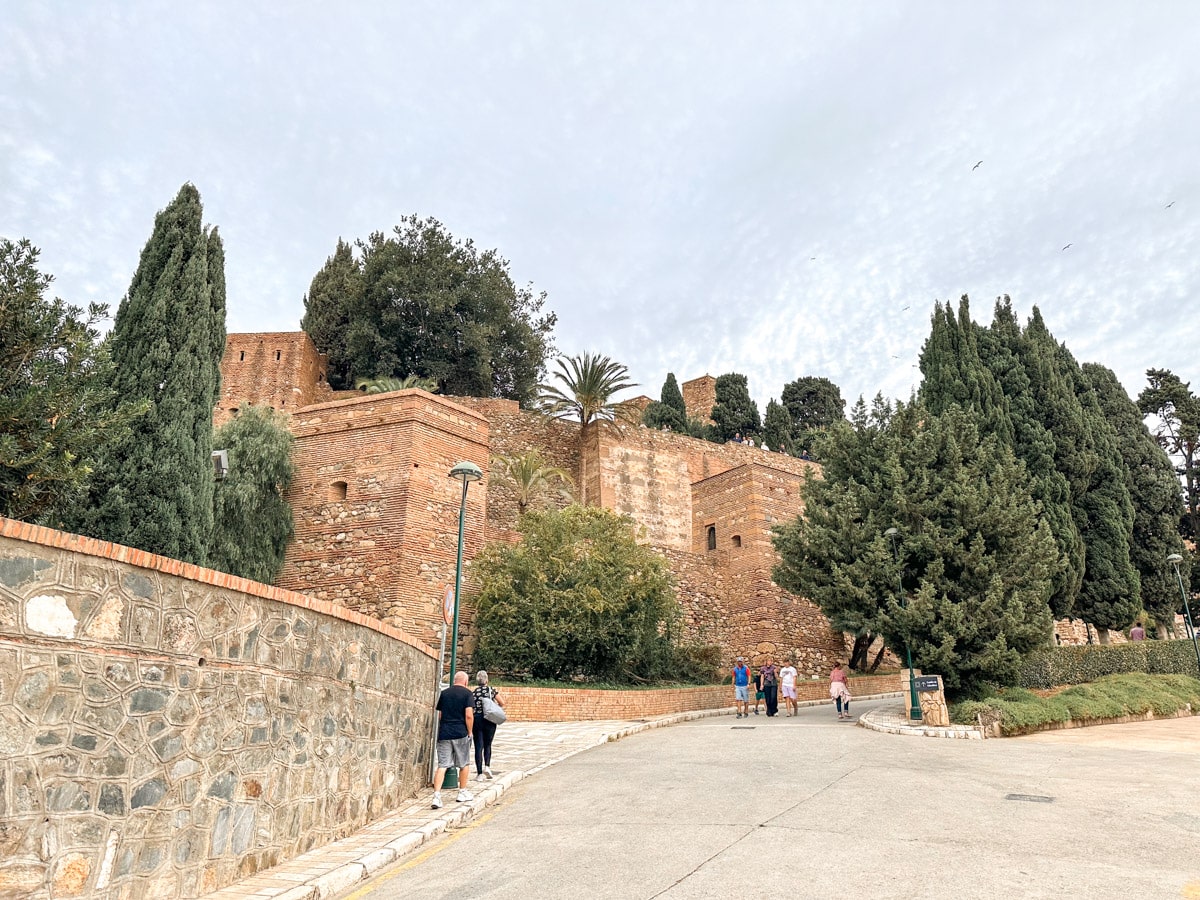 The ancient Alcazaba of Málaga, a fortified Moorish palace with verdant trees and people strolling by.