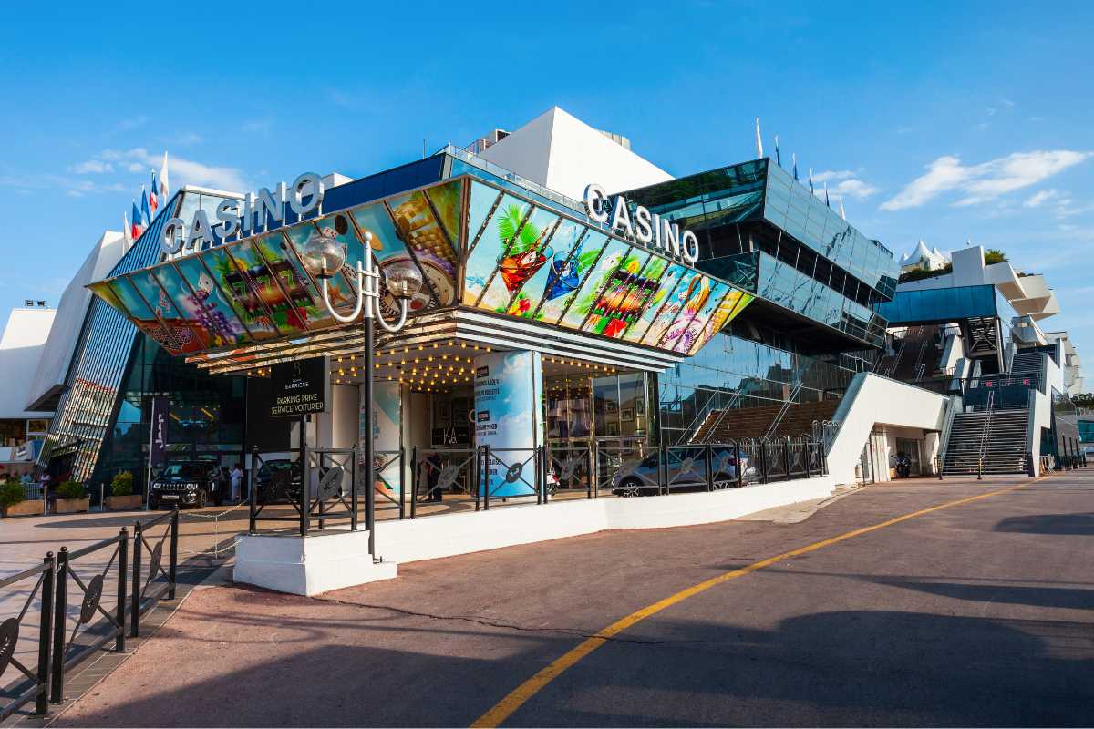 The modern facade of the Casino Barrière in Cannes, featuring a vibrant, artistic entrance, with a clear sky above and a quiet esplanade in front.