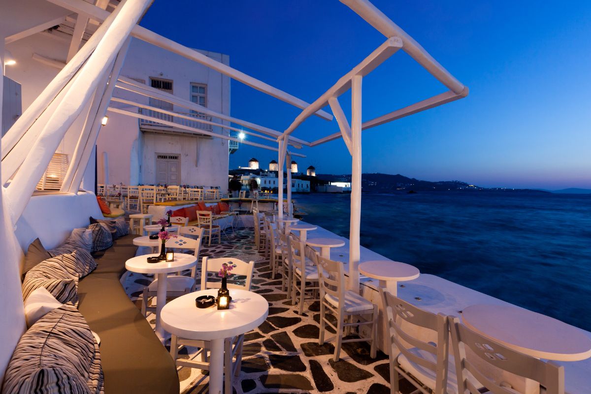 A cute empty bar in Mykonos in the evening with a view of the ocean and the windmills in the background. The nightlife is one of the biggest reasons why Mykonos is worth visiting.