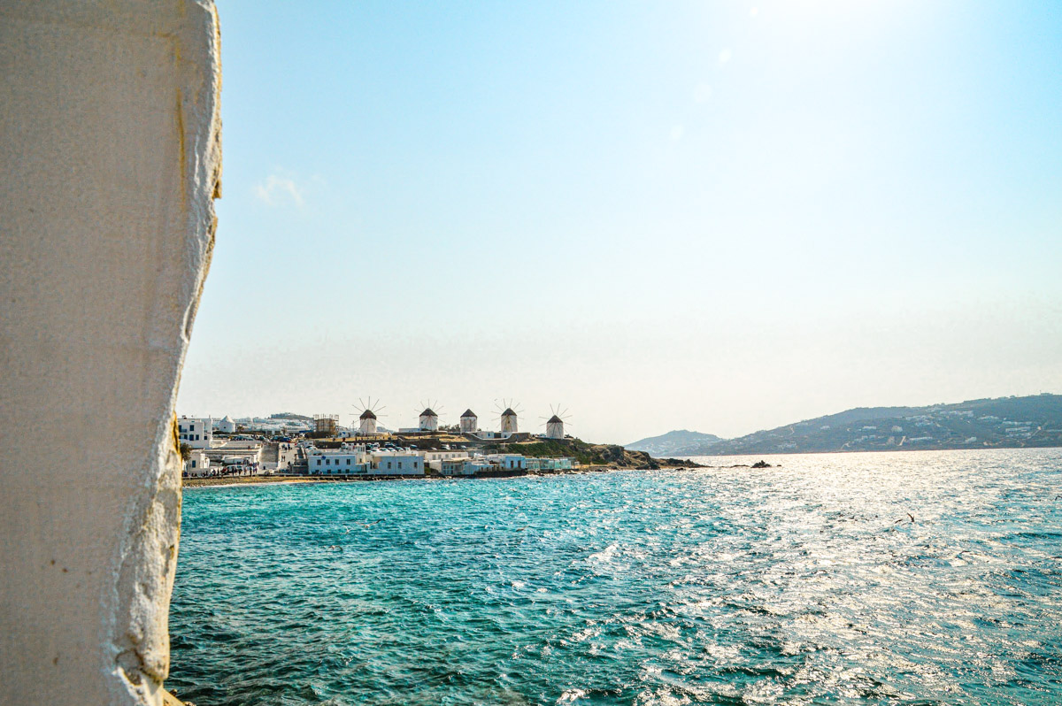 A picturesque view of the Mykonos windmills against a bright blue sky, overlooking the sparkling sea, reflecting the island's history and charm.