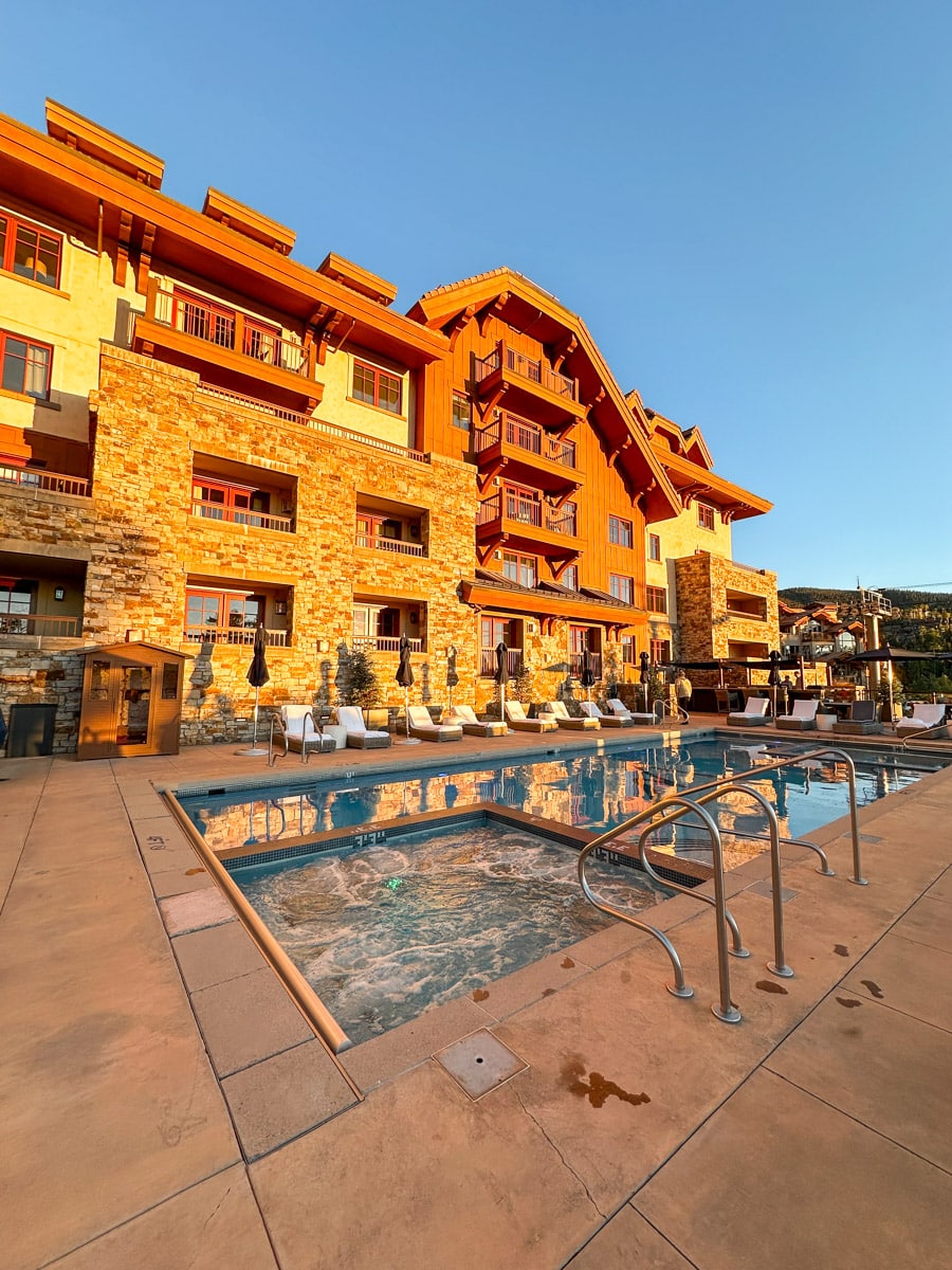A luxurious pool area with mountains in the background during sunset, showing loungers and umbrellas.
