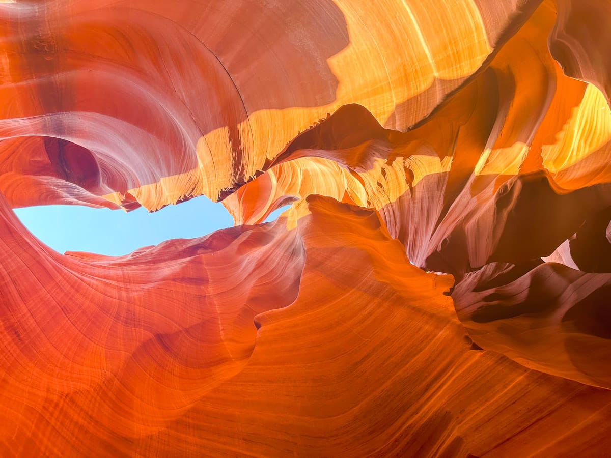 The smooth, flowing sandstone curves inside a slot canyon, illuminated with vibrant shades of orange and red, under a blue sky