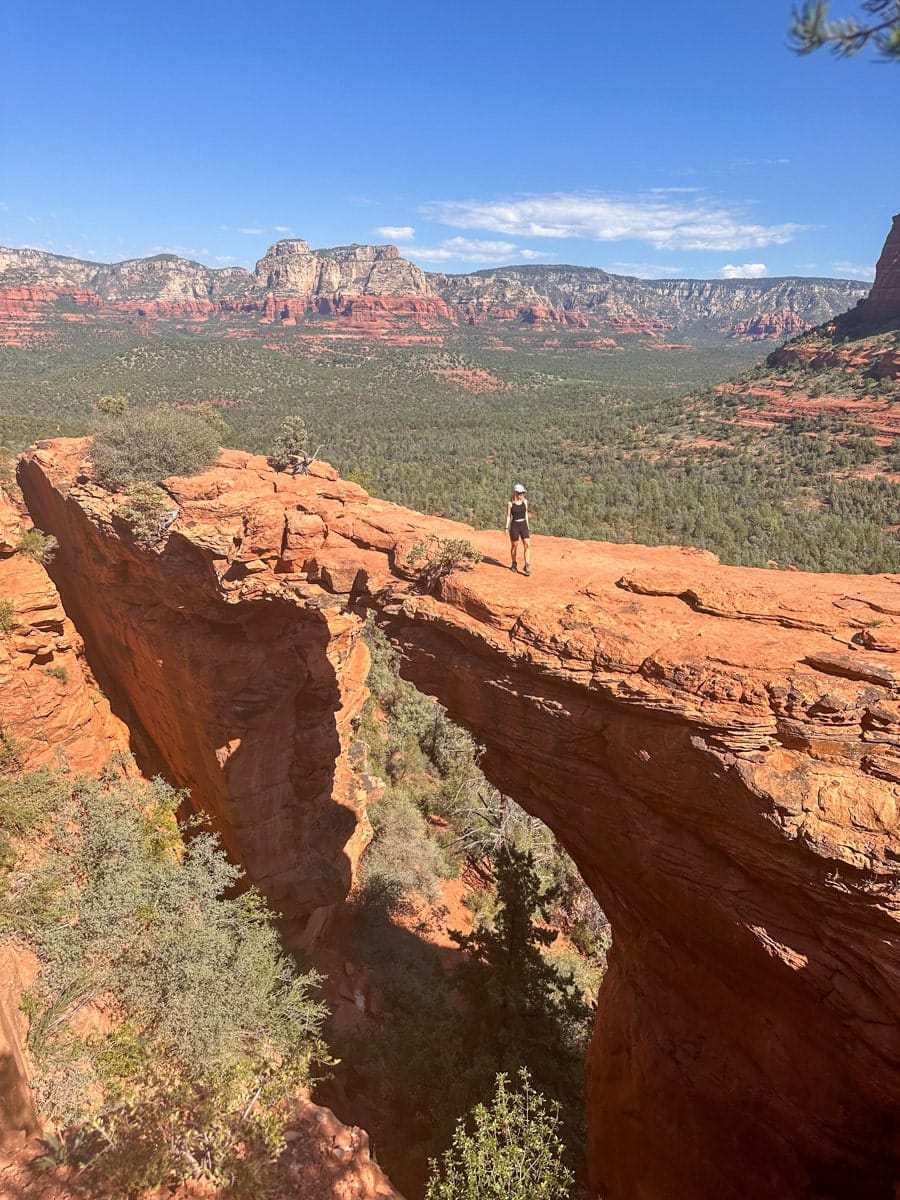 the author's wife standing on Devil's Bridge in Sedona, a red rock natural arch, with sweeping views of the surrounding desert landscape.