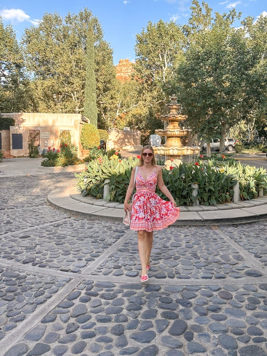 the author's wife in a colorful summer dress posing by a charming courtyard fountain in Sedona, Arizona, surrounded by trees and greenery.