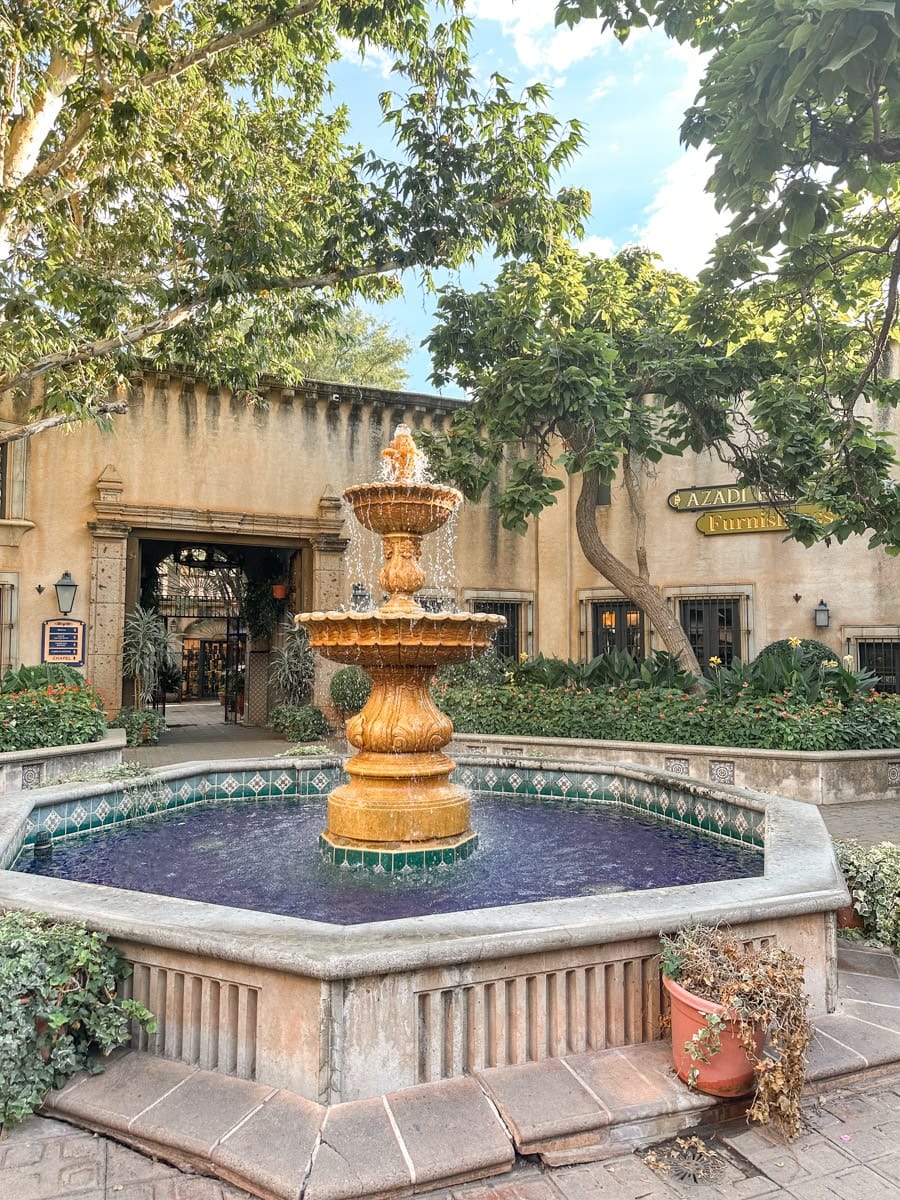 A golden-tiered fountain surrounded by lush plants in a quaint Sedona courtyard under a blue sky.