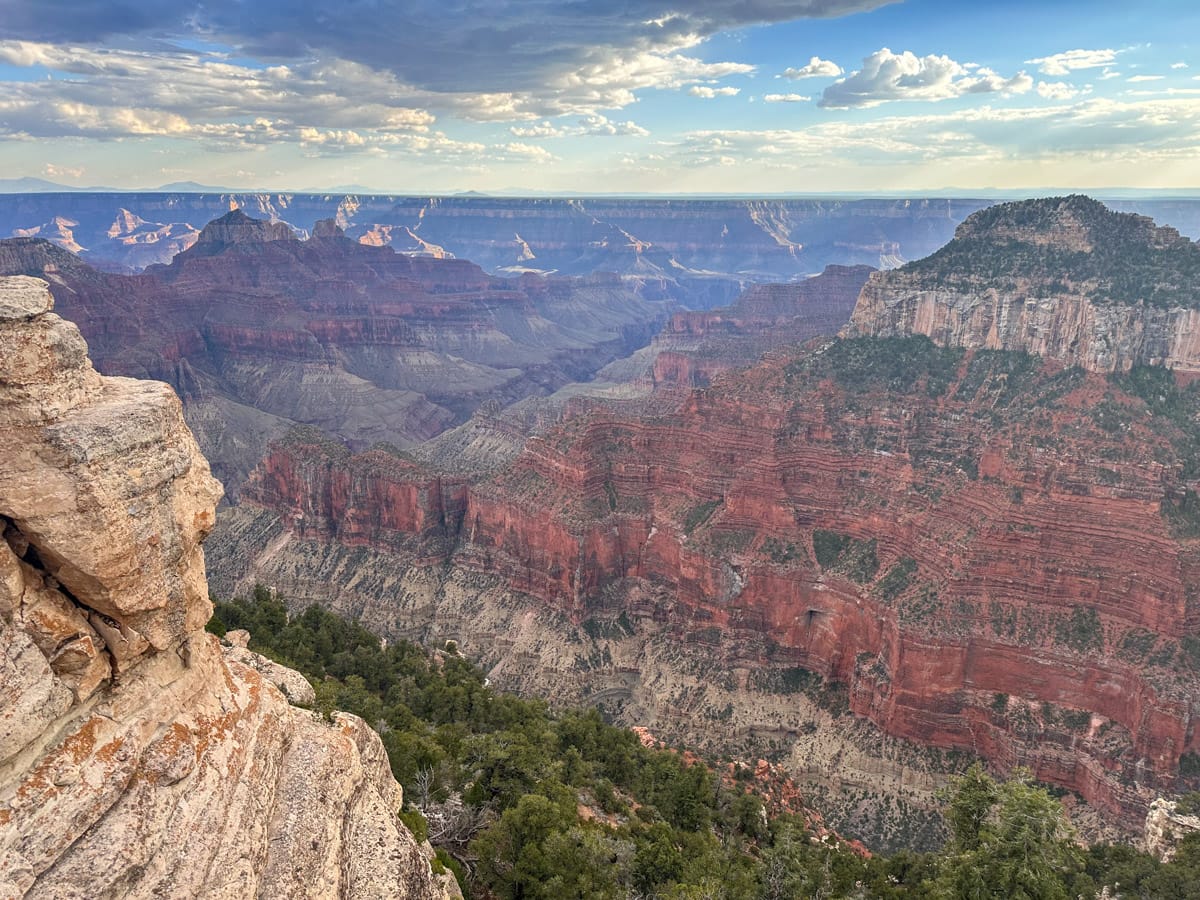 A panoramic view of the Grand Canyon with towering red rock formations and deep valleys under a partly cloudy sky.