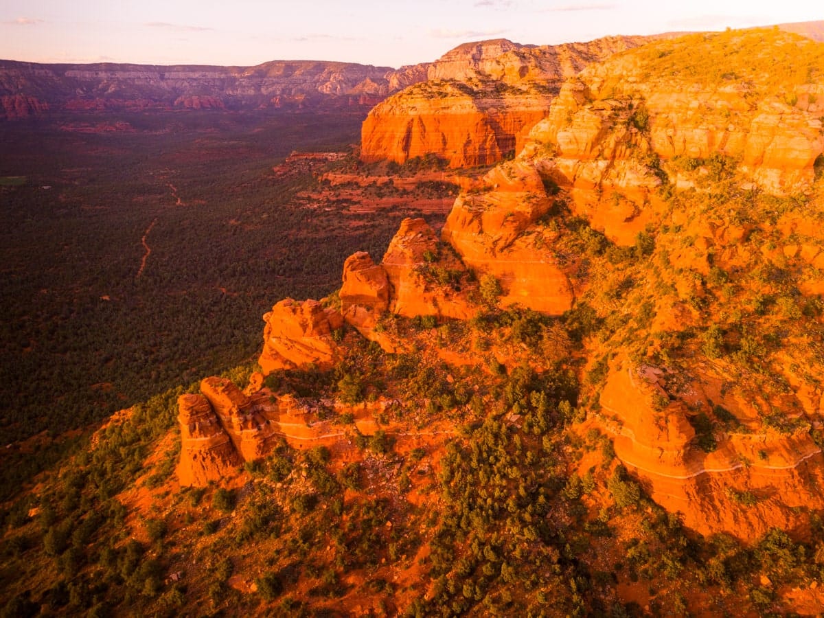 Aerial view of Sedona's vibrant red rock formations bathed in the warm light of sunset, with a vast desert landscape in the background.