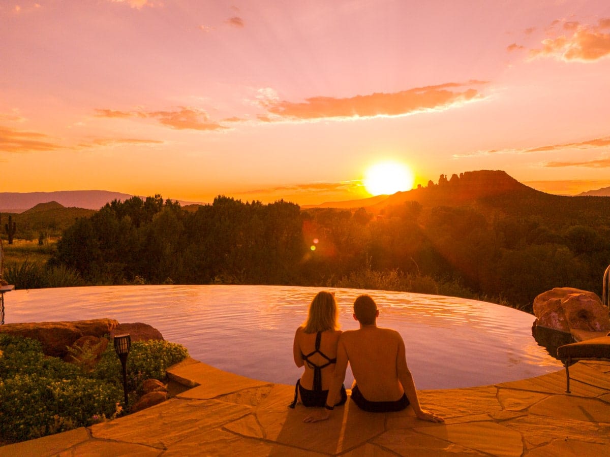 A couple sitting by an infinity pool in Sedona, Arizona, watching a breathtaking sunset over the red rocks and desert landscape.
