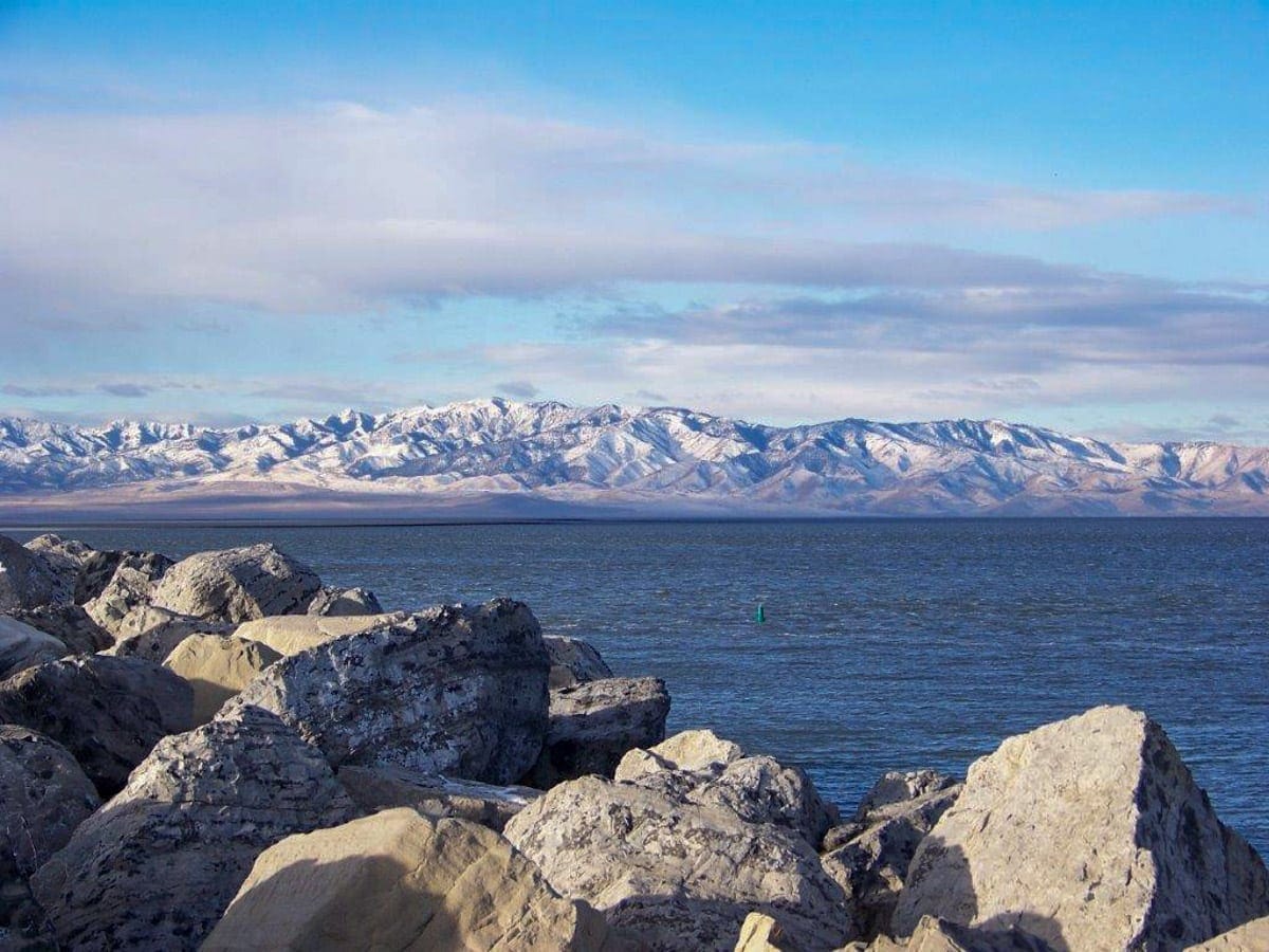 The shoreline of the Great Salt Lake with large boulders in the foreground and snow-capped mountains in the distance
