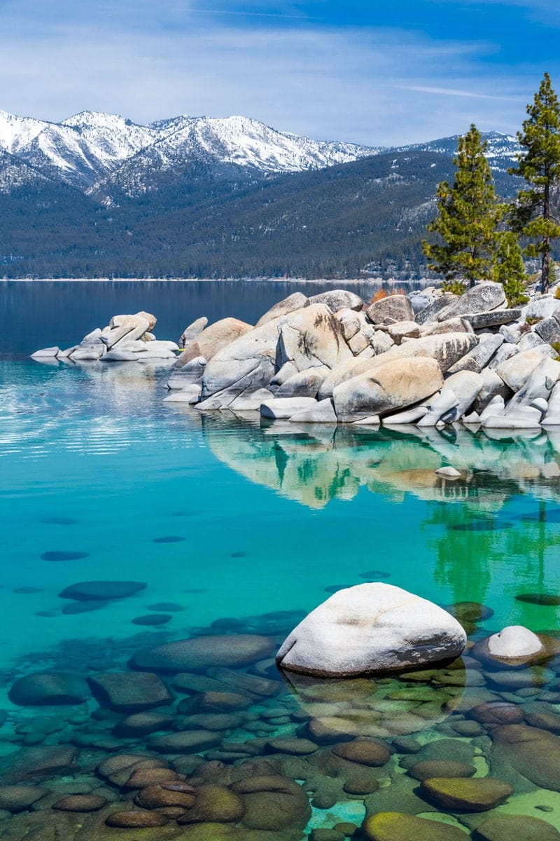 Crystal-clear turquoise waters of Lake Tahoe reflecting snow-covered mountains and pine trees on a bright winter day.