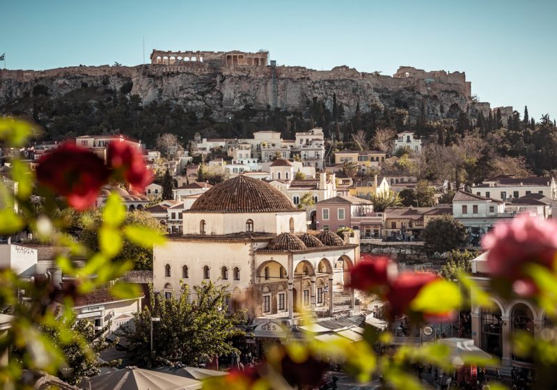 A breathtaking cityscape of Athens, highlighting the Acropolis on the hill with flowers framing the foreground.