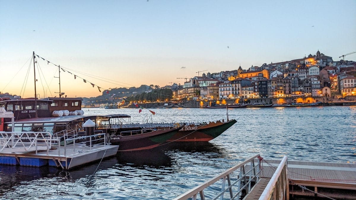 Sunset on the Douro River – A beautiful twilight view of Porto’s riverside with boats docked along the waterfront, city lights reflecting on the water.