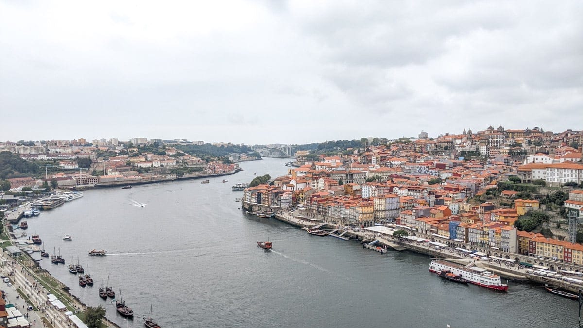 Aerial view of Porto and the Douro River – A panoramic shot capturing the red-roofed buildings of Porto along the winding Douro River, with traditional boats navigating the waterway.