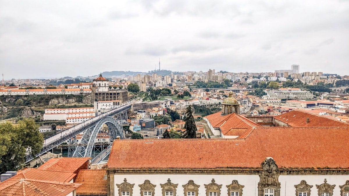 Rooftop view of Porto and Dom Luís I Bridge – A scenic perspective from a high vantage point, showcasing the city’s terracotta rooftops, a historic monastery, and the famous bridge stretching across the river.