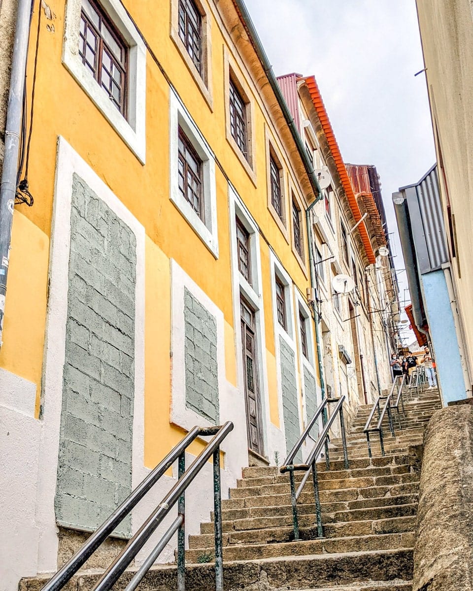 Steep stairway in Porto’s old town – A classic Portuguese street scene with a long flight of stone stairs leading up past rustic yellow buildings with shuttered windows.