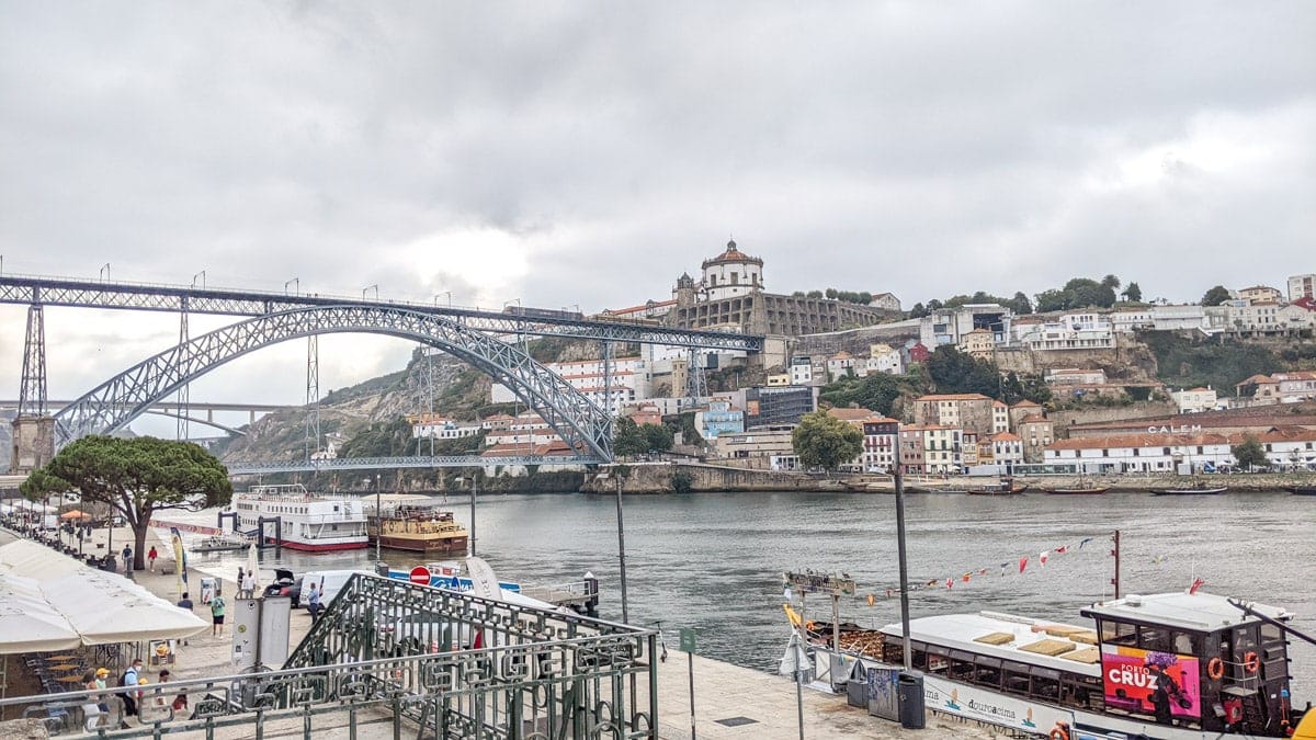 Riverfront promenade in Porto – A lively riverside walkway with bustling cafés, boats docked along the water, and the grand Dom Luís I Bridge in the distance.