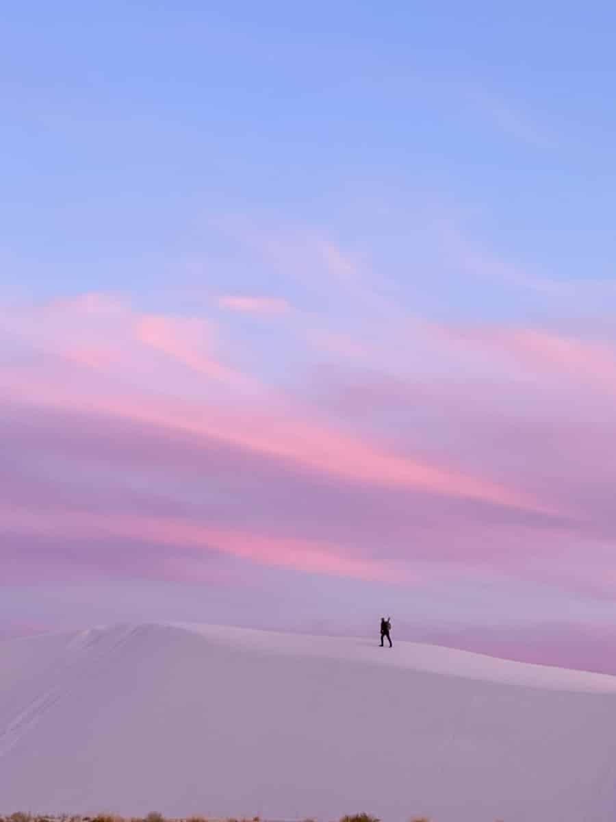 the author hiking up a white sand dune at sunset with a pink sky