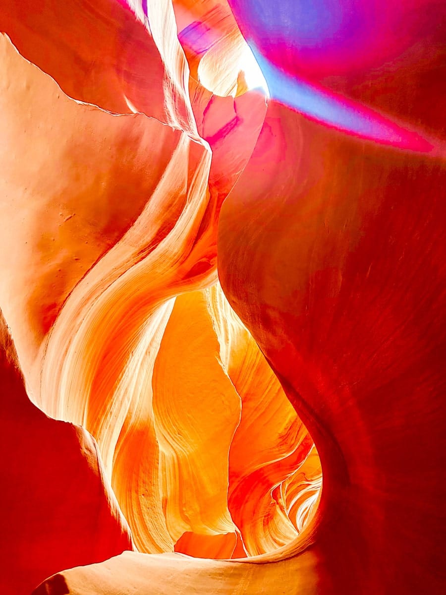 Vibrant light beams shine through the narrow, wavy walls of Antelope Canyon in Arizona. The swirling sandstone glows in fiery shades of red, orange, pink, and gold, creating an otherworldly scene that showcases the canyon’s famous curves and textures.