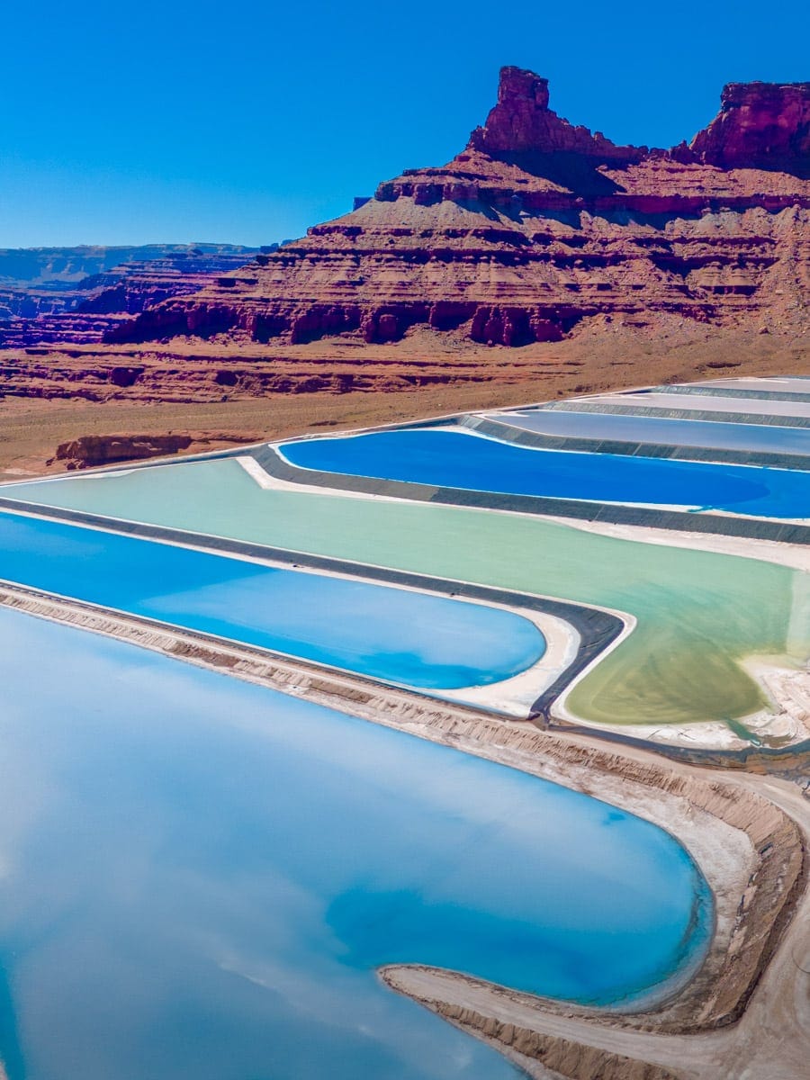 Vibrant blue and green potash evaporation ponds near Moab, Utah, appear like abstract art against the arid desert terrain. The geometric patterns of the pools are striking against the backdrop of red rock mesas and buttes.