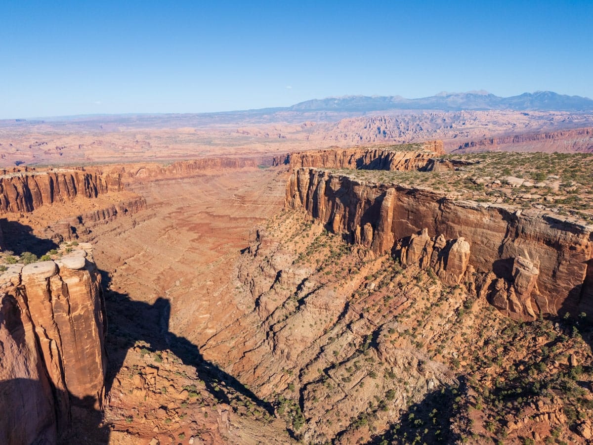 Striking layers of red, orange, white, and gray rock create a dramatic geological formation in Capitol Reef National Park, Utah. The towering cliffs and striped hills tell a story of ancient sediment, with the vibrant hues glowing under bright desert sunlight.