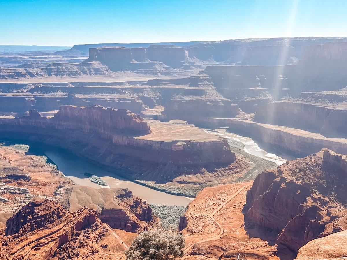 A breathtaking view over the deep canyons of Dead Horse Point State Park in Utah, showing a winding stretch of the Colorado River carving through layered red rock mesas. A sunbeam cuts across the scene, adding a magical glow to this dramatic desert overlook.