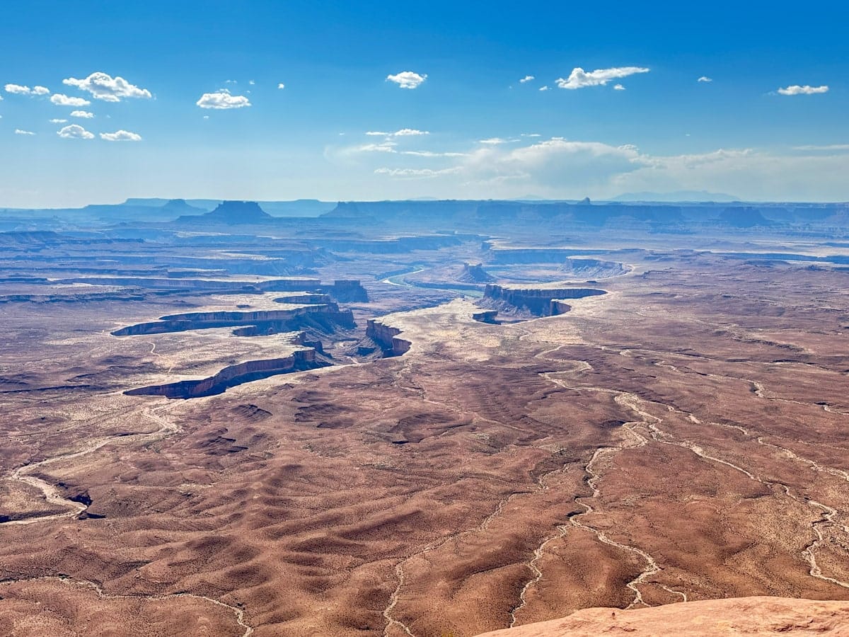Epic panoramic view of Canyonlands National Park, with deep canyons and winding riverbeds stretching across a dramatic, rugged desert landscape.