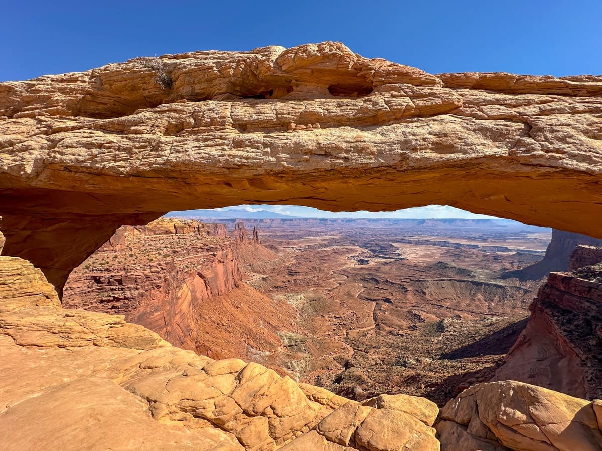 The breathtaking Mesa Arch in Canyonlands National Park frames a sweeping canyon view, with layered red rock formations glowing under the midday sun.